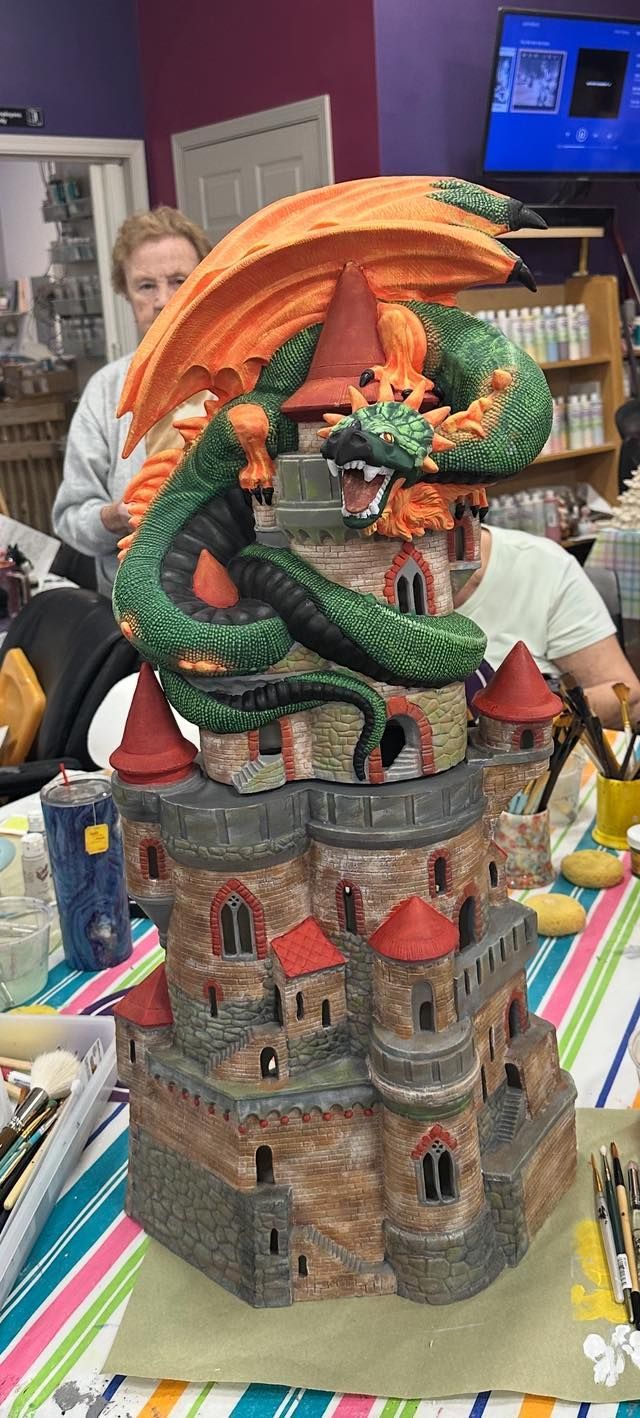 A ceramic castle figurine with a green dragon and orange wings, people in background.