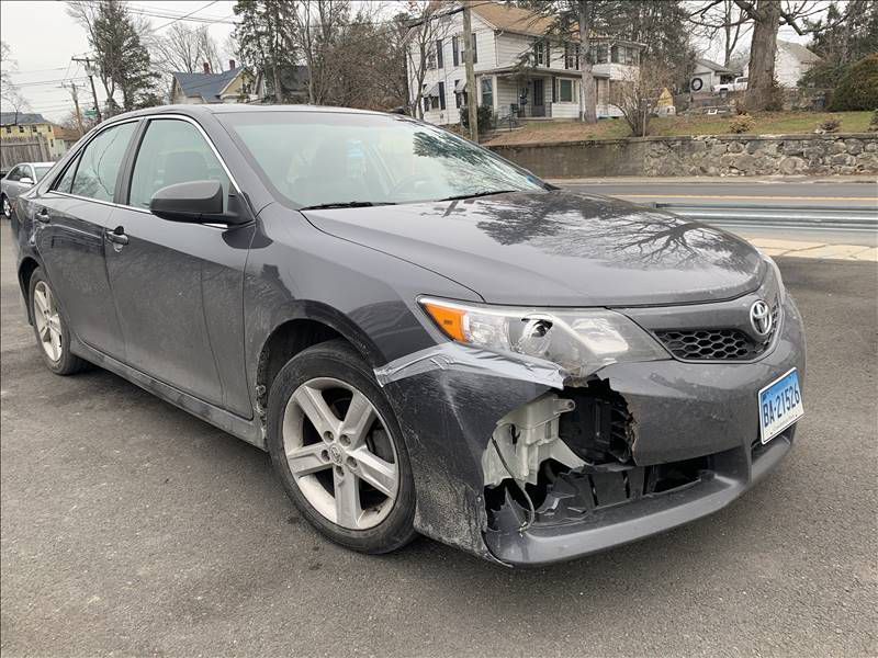 A gray car with a damaged front end is parked on the side of the road.