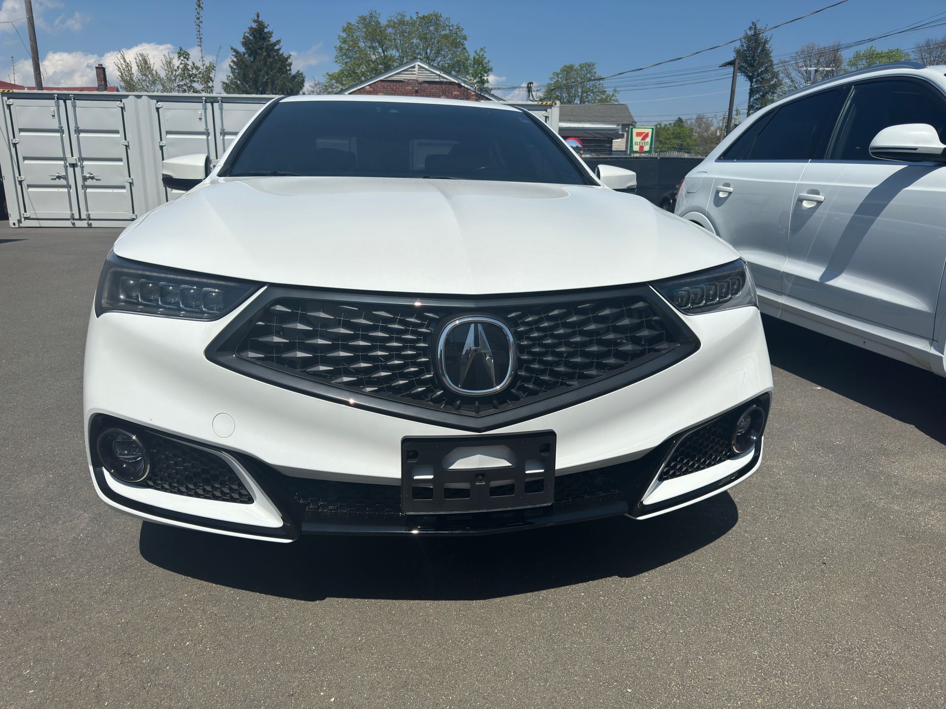 A white acura integra is parked in a parking lot next to a silver car.
