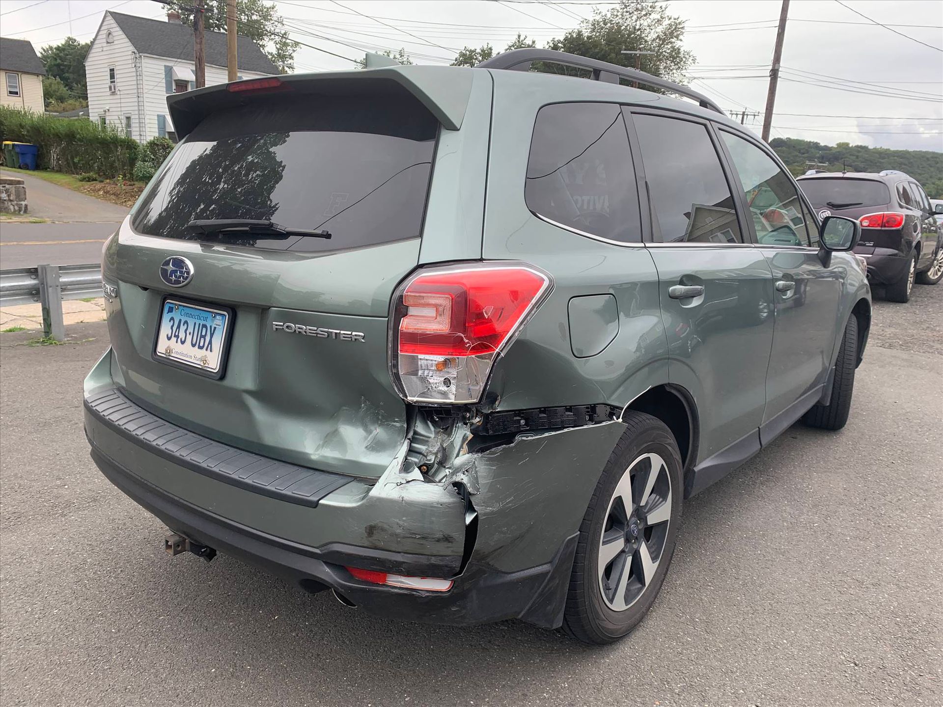 A subaru forester with a damaged rear end is parked on the side of the road.