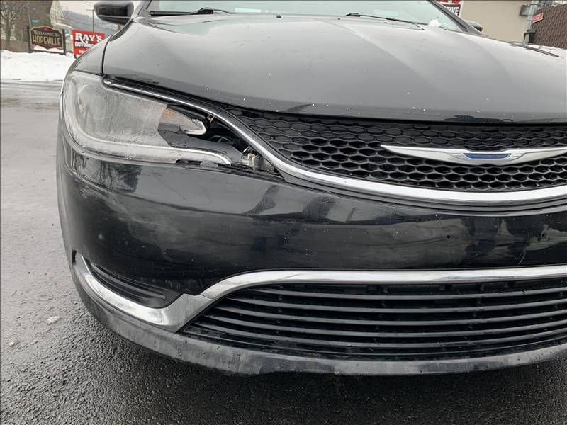 A black car with a broken headlight is parked on the side of the road.