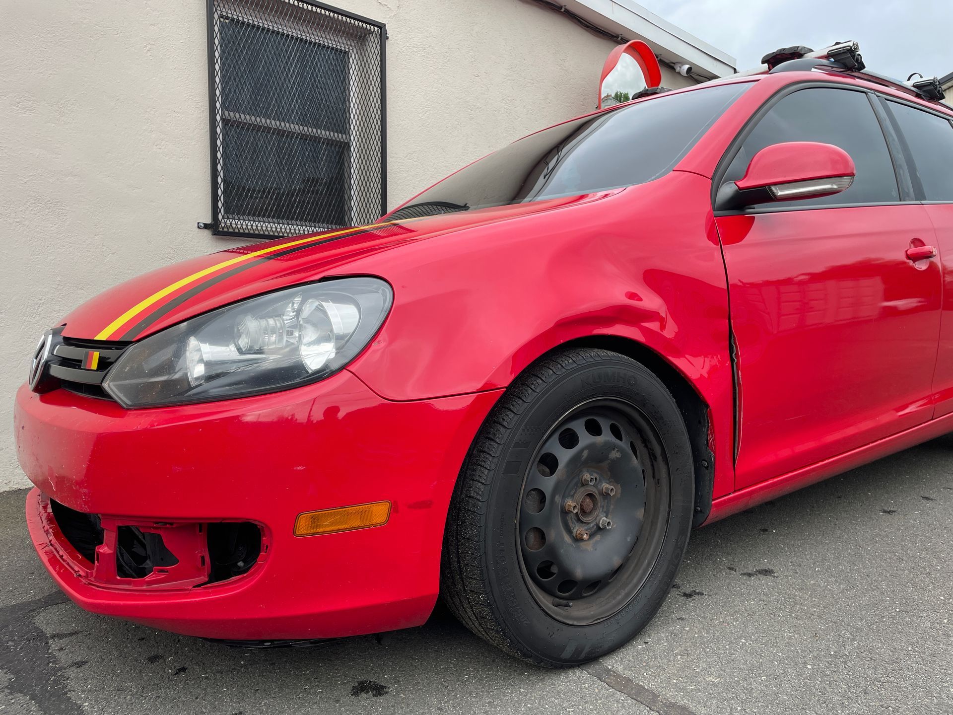A red car with a yellow stripe on the side is parked in front of a building.