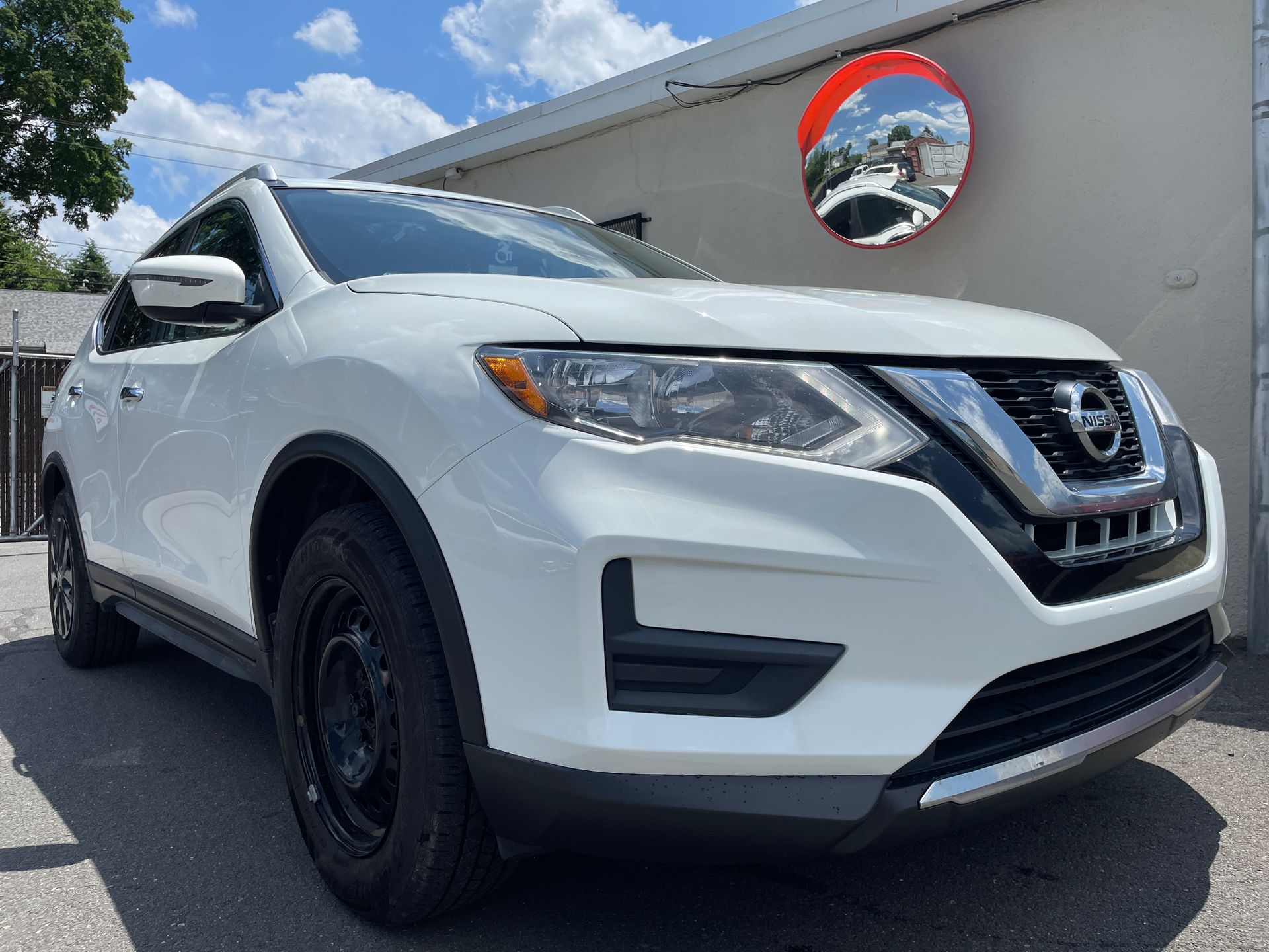 A white nissan rogue is parked in front of a building.