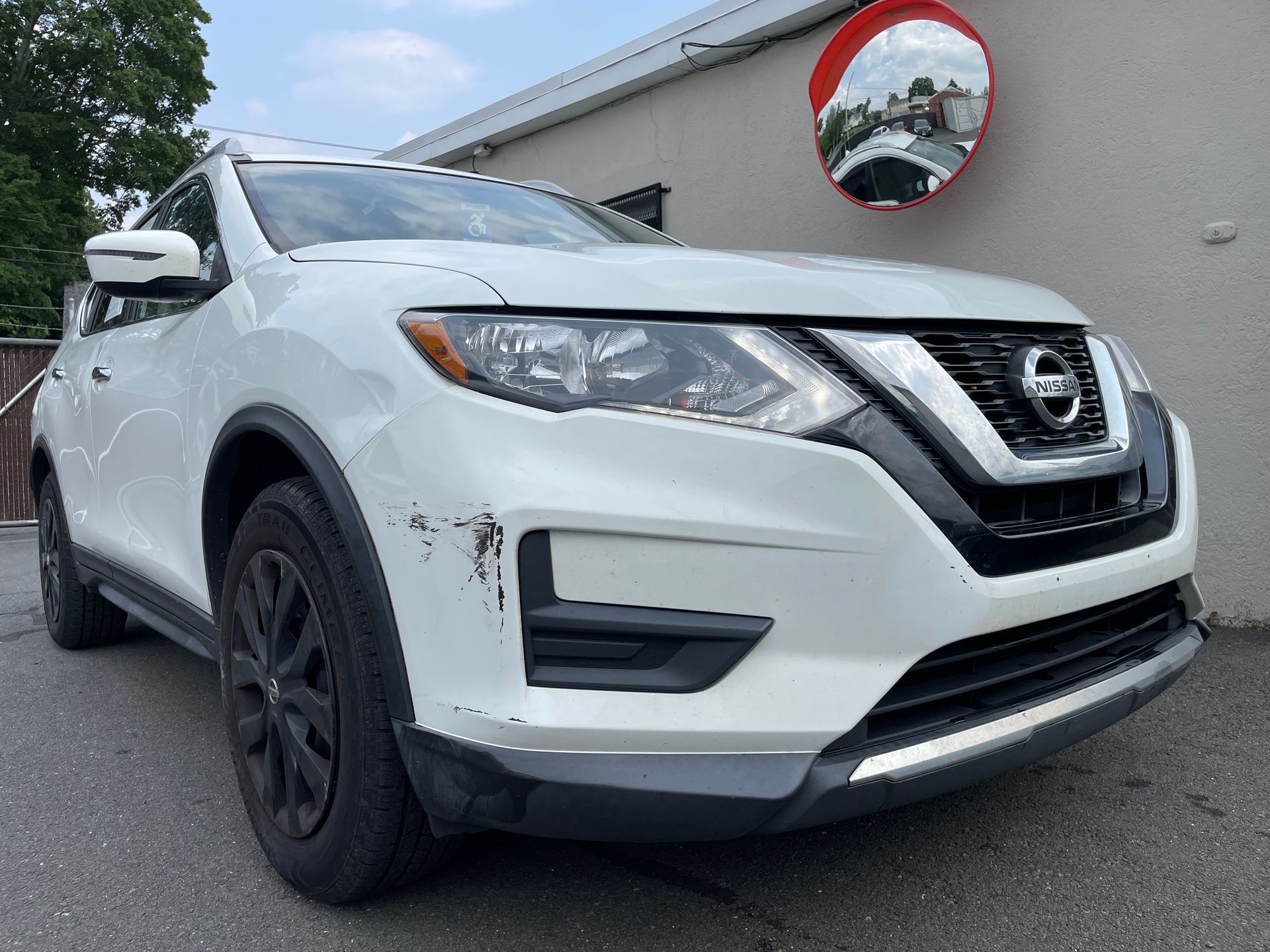 A white nissan rogue is parked in front of a building.