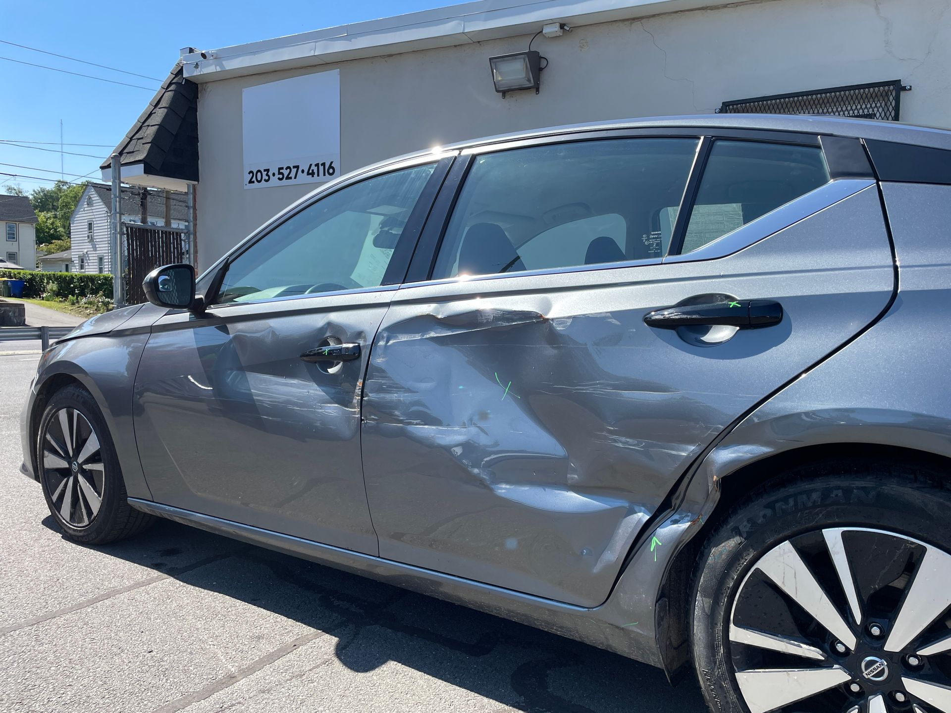 A gray car with a damaged side is parked in front of a building.