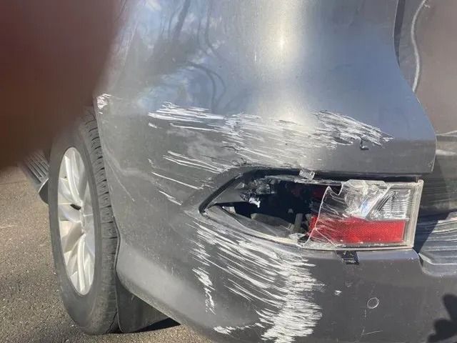 A grey car with a damaged bumper and tail light.