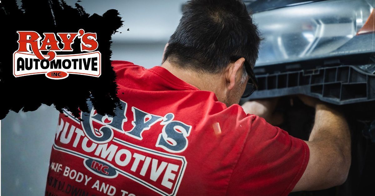 A mechanic wearing a red shirt with Ray's Automotive branding works on the front headlight assembly of a vehicle.