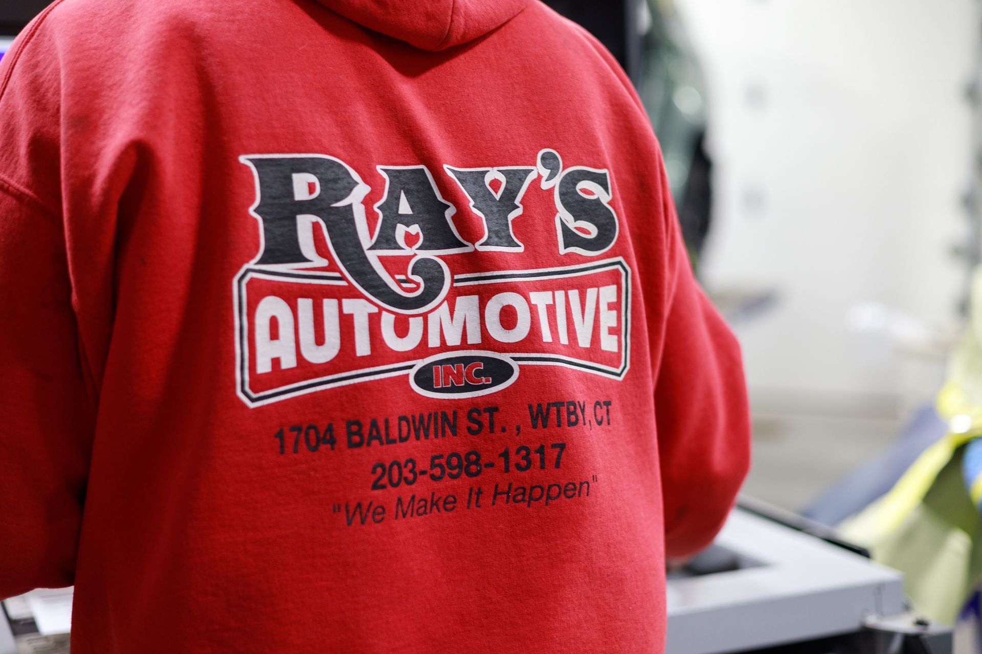 Person in red shirt with Ray's Automotive logo on back, standing indoors near equipment