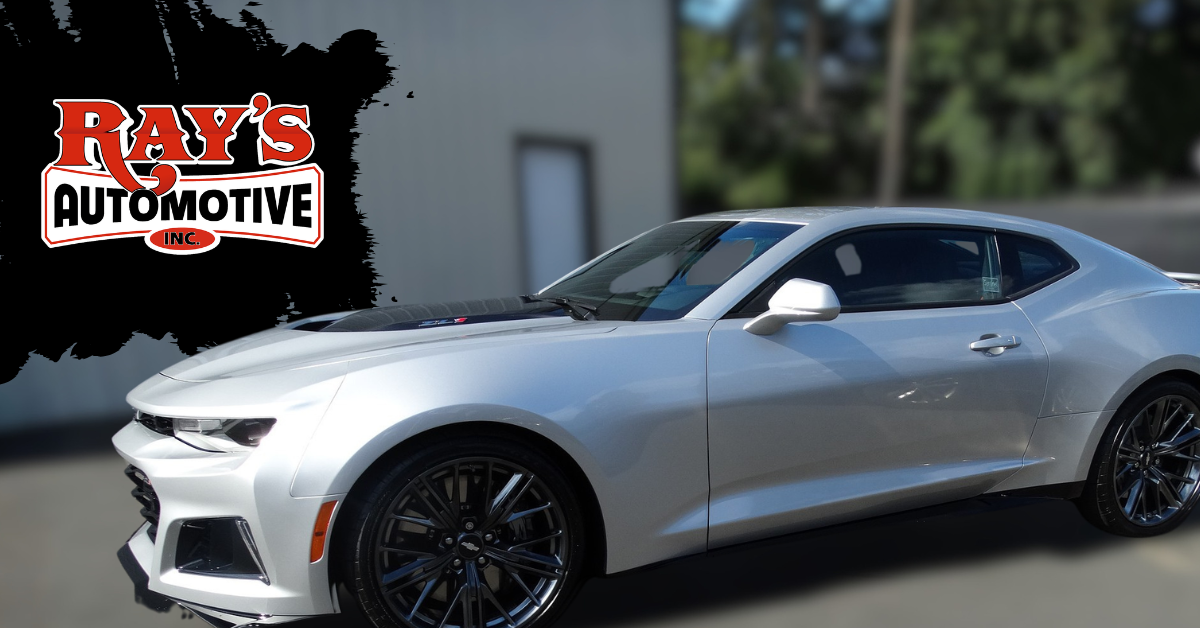 A silver Chevrolet Camaro parked on an asphalt lot beside a building.