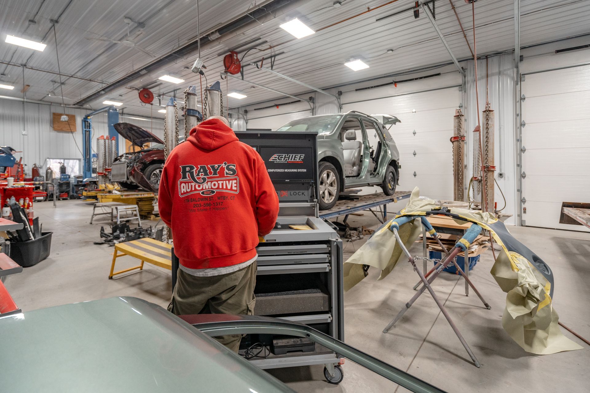 Auto repair shop interior with a person in a red hoodie near a vehicle under repair