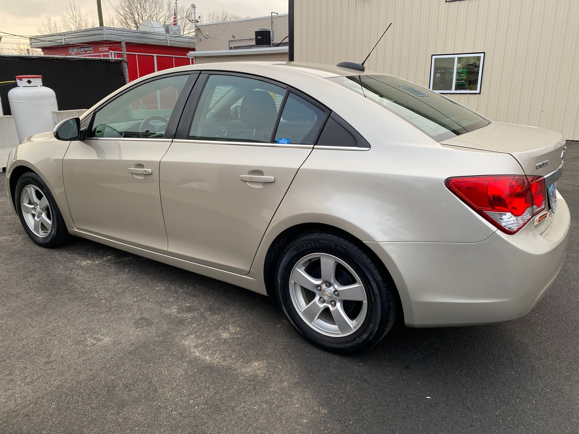 A beige chevrolet cruze is parked in front of a building.