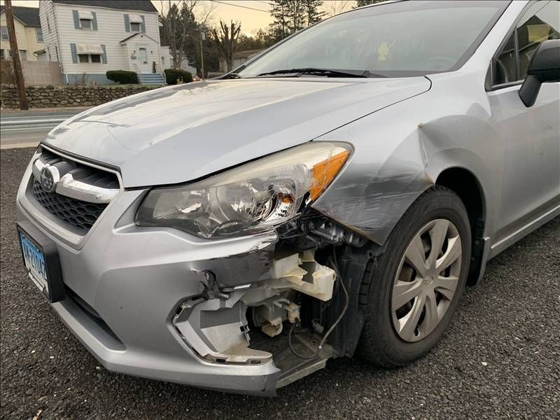 A silver car with a damaged front end is parked in a parking lot.