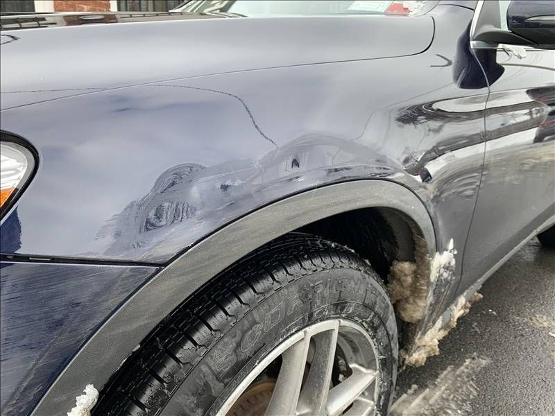 A blue car with a damaged fender is parked on the side of the road.