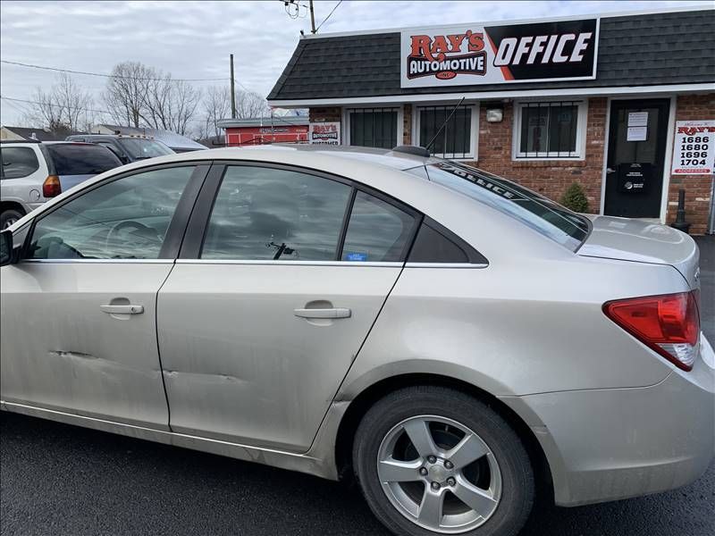 A beige chevrolet cruze is parked in front of a building.