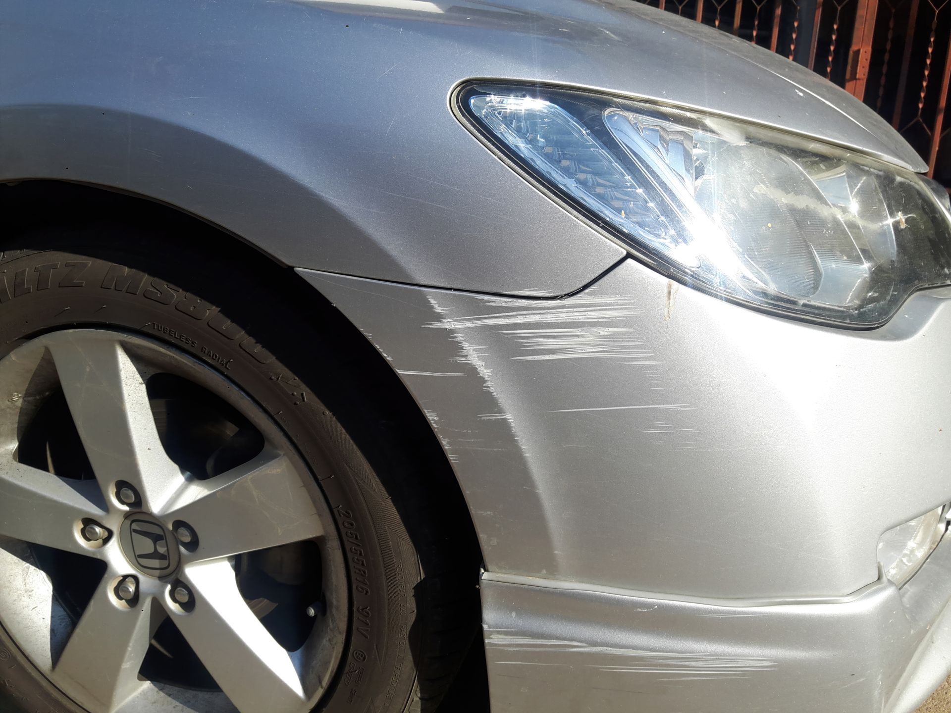 A silver car with a scratch on the front bumper.
