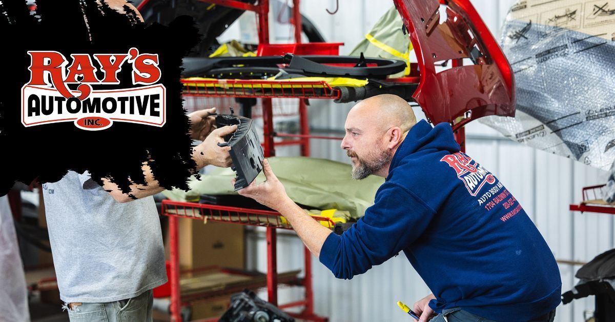 Two people in an auto shop workspace examine a dark vehicle component together.