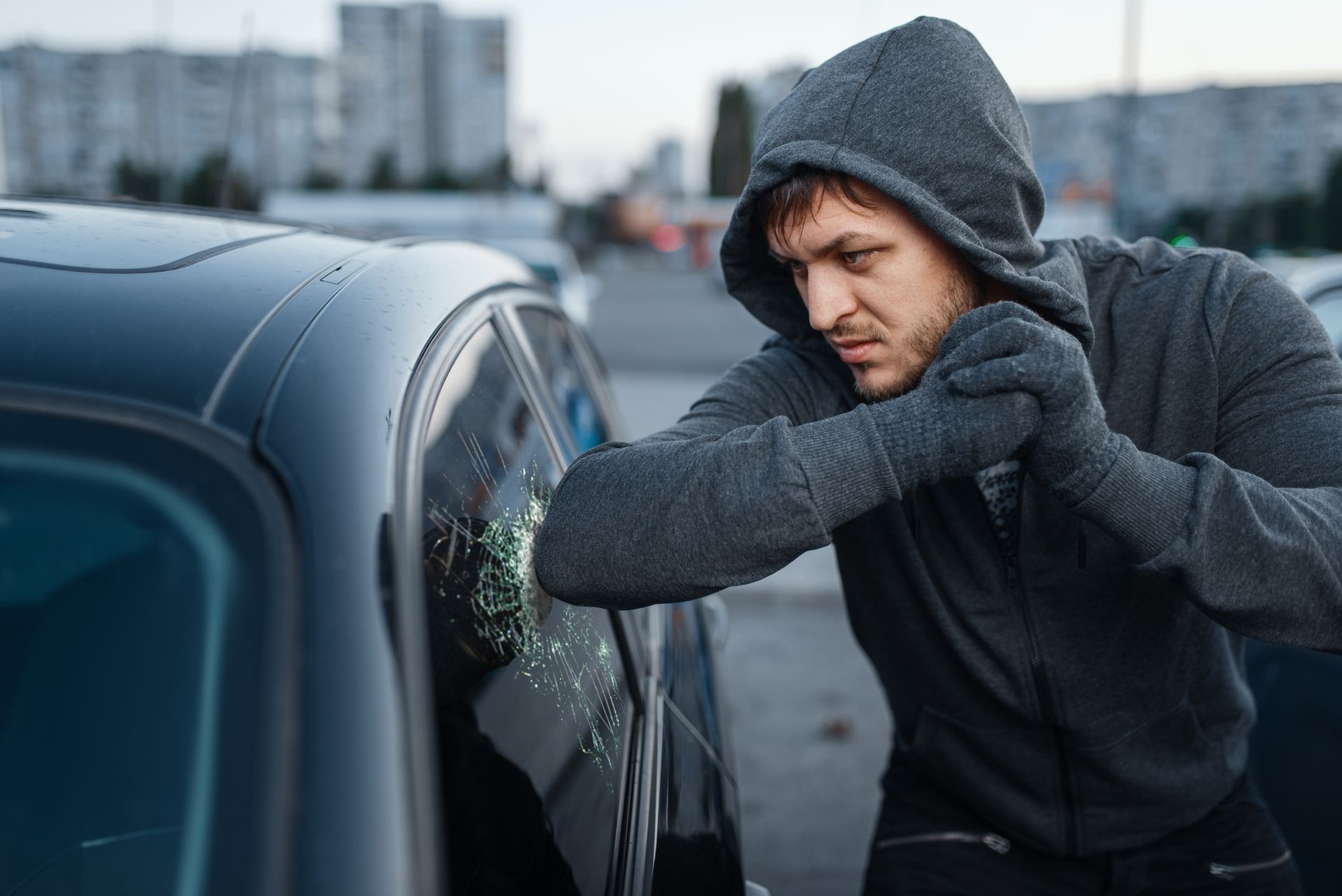 A man in a hoodie is breaking into a car.

