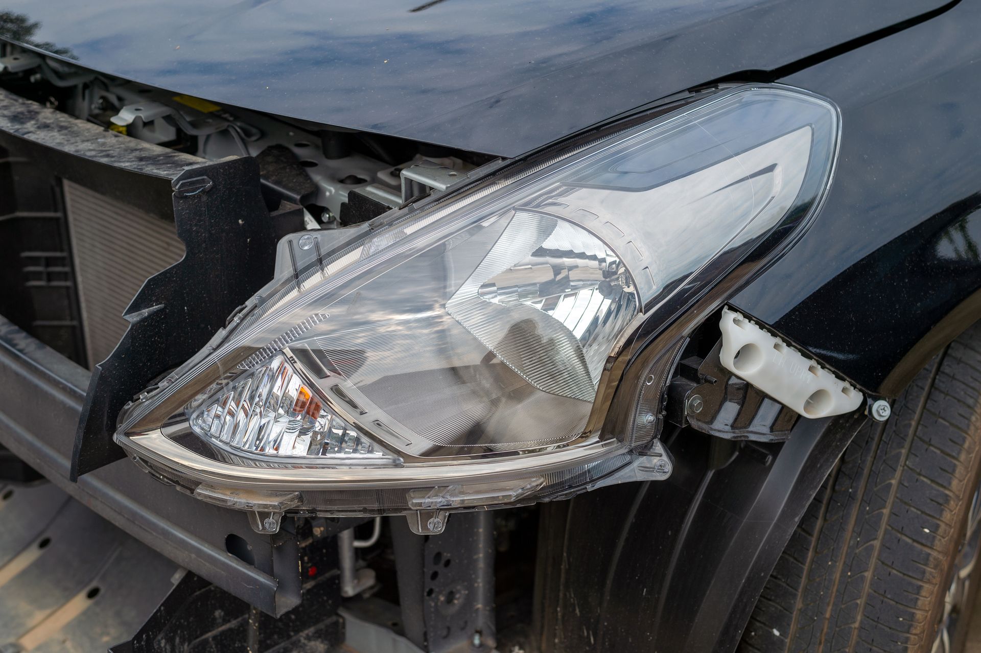 Damaged car headlight and front bumper with visible collision damage and missing grille