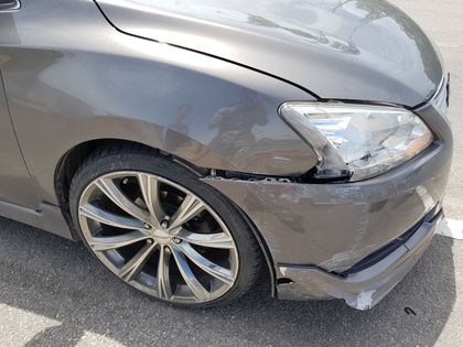 A car with a damaged bumper is parked on the side of the road.
