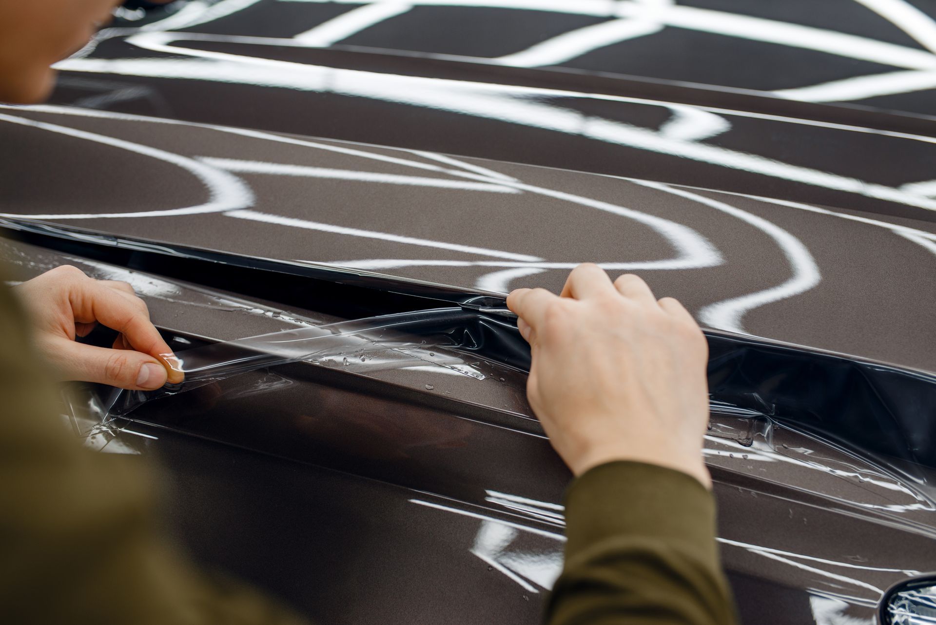 A person is applying a protective film to the hood of a car.
