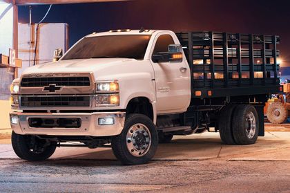 A white truck with a wooden bed is parked in a parking lot at night.
