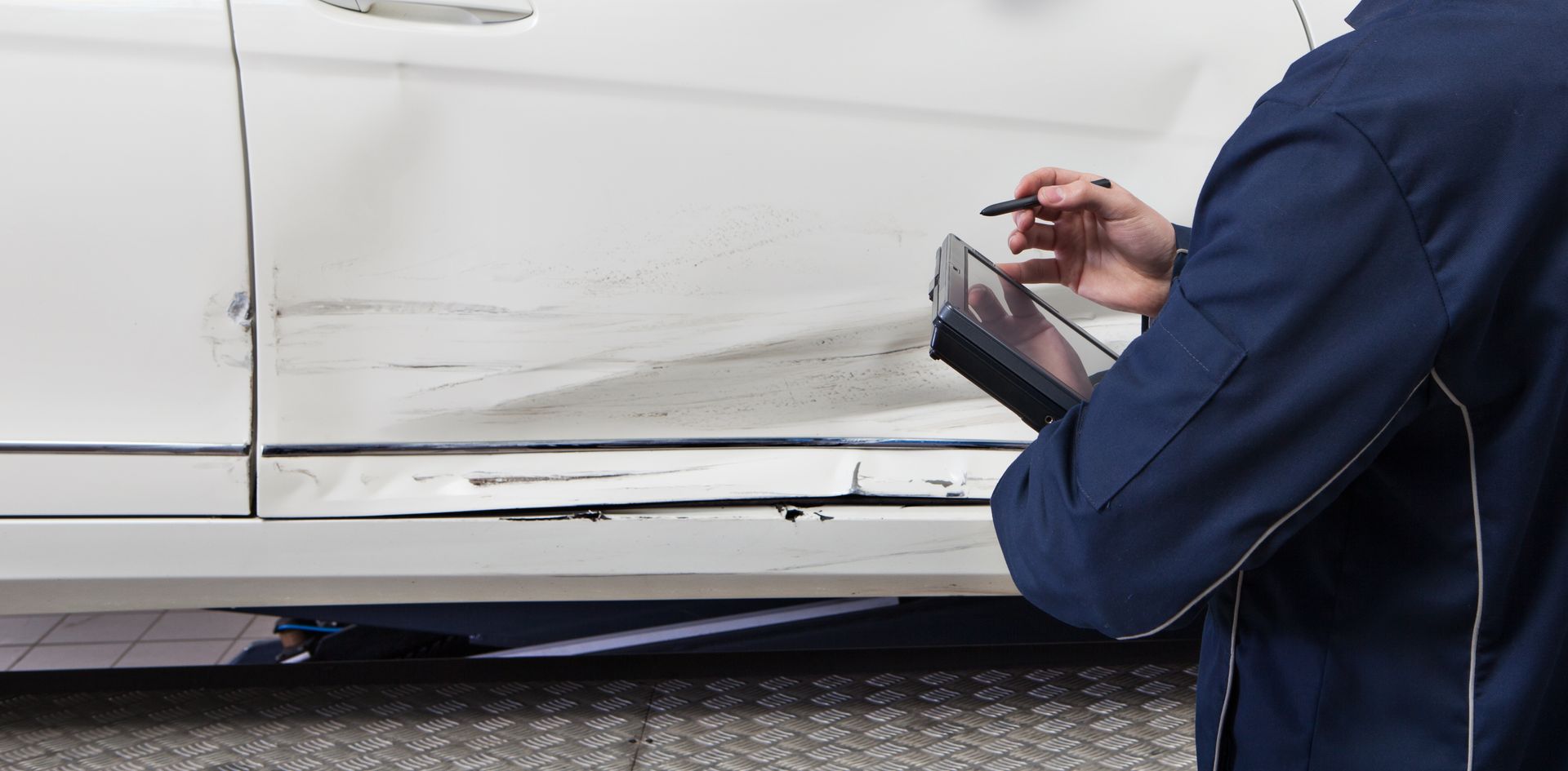 A man is writing on a clipboard in front of a white car.
