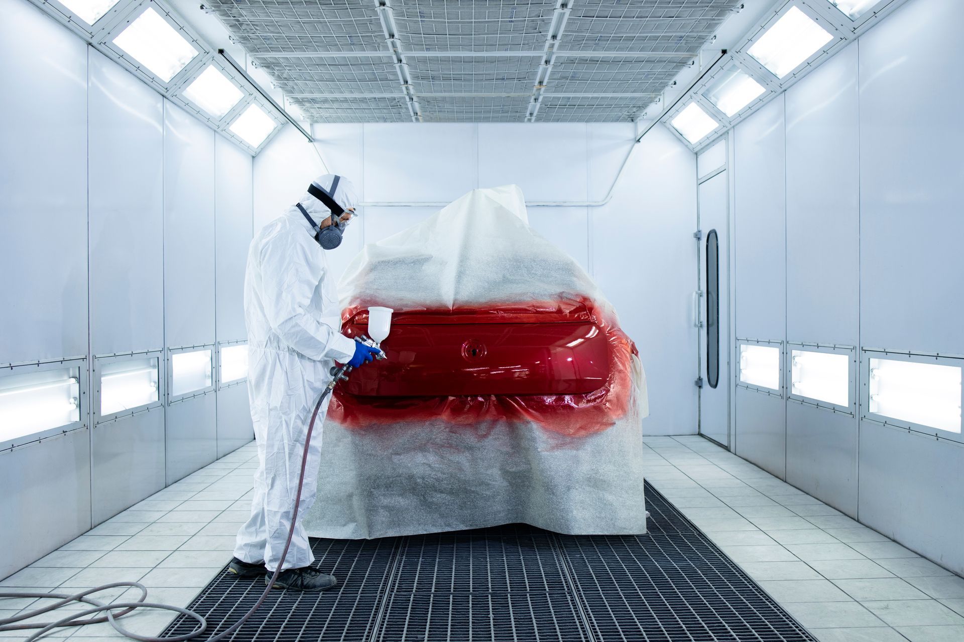 A man is painting a car in a paint booth.
