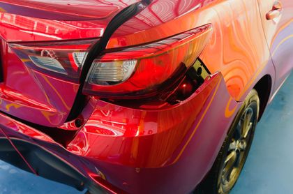 A red car with a damaged bumper is parked on a blue floor.
