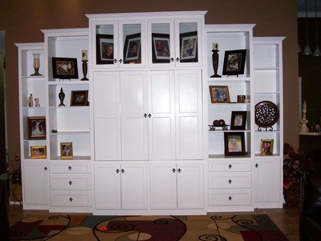 Built-in white living room cabinets with shelves, drawers, and framed photos above a patterned rug.