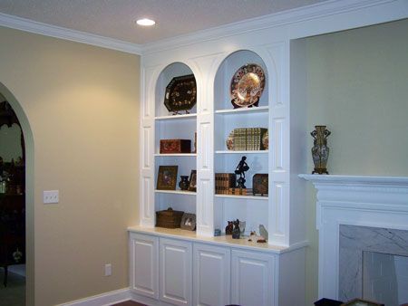 Built-in wall shelves with decor beside a white fireplace in a beige living room