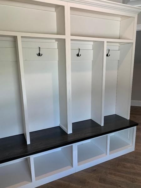 White built-in mudroom cubbies with hooks and a dark bench seat beneath a shelf.