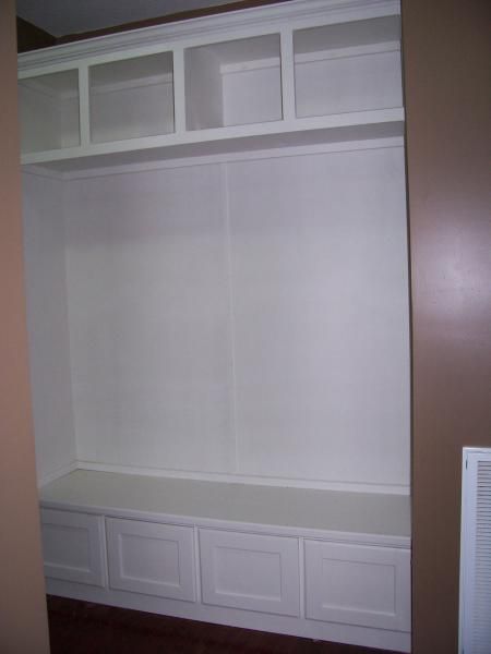 Built-in white closet with shelves, drawers, and a central hanging space against a beige wall.