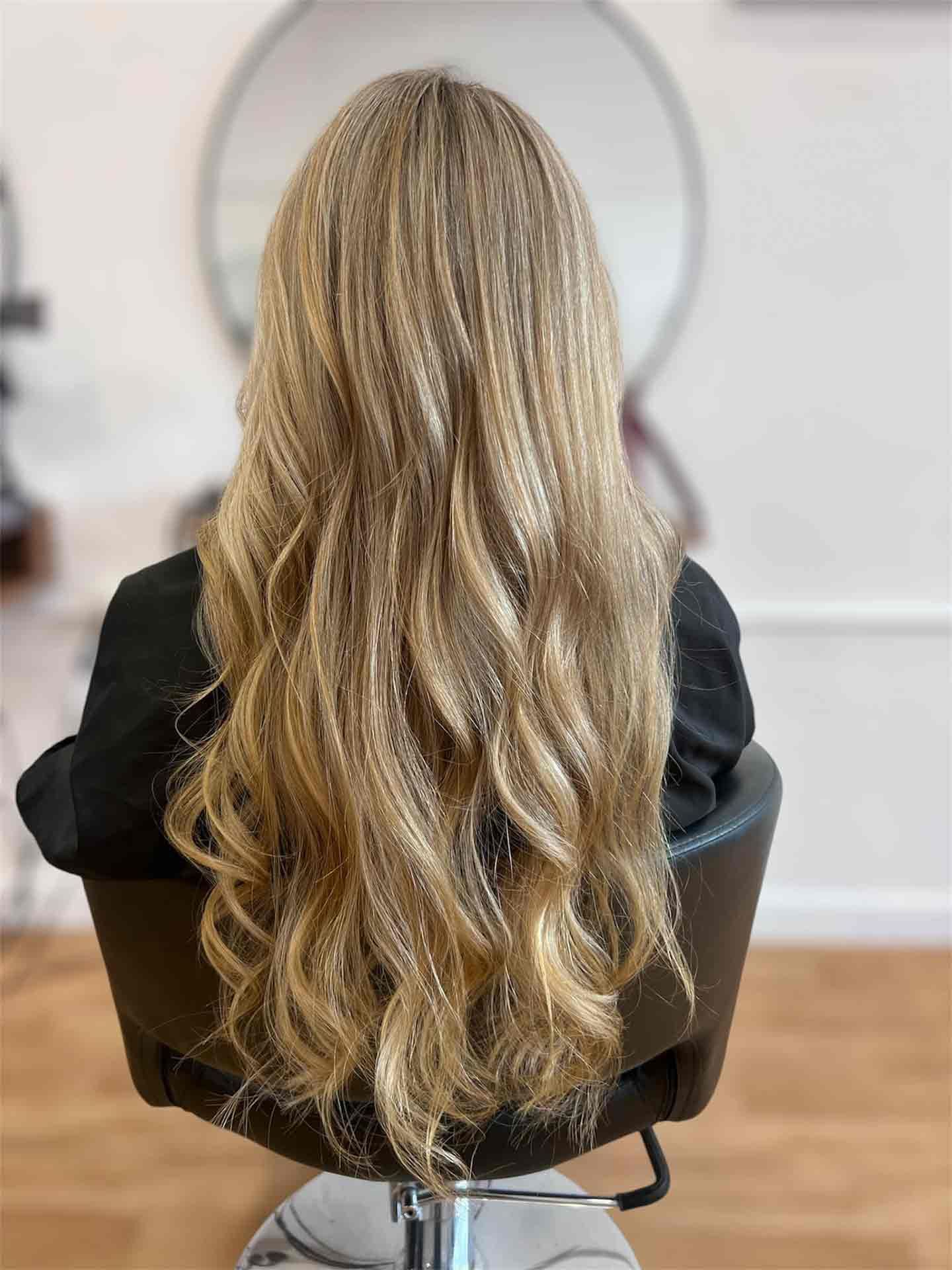 A Woman With Long Blonde Hair Is Sitting In A Chair In A Salon — Mjay's Hair Studio & Spa In Dubbo, NSW