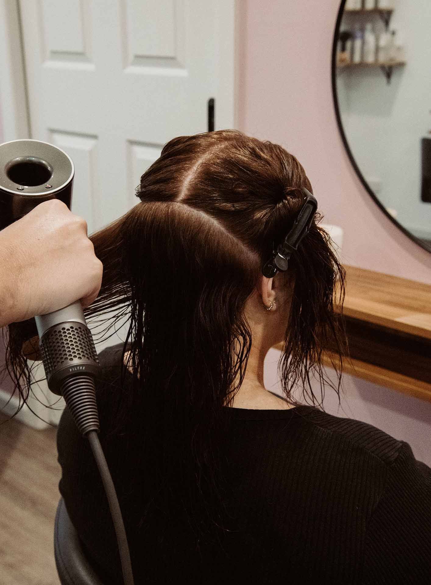 A Woman Is Getting Her Hair Blow Dried In A Salon — Mjay's Hair Studio & Spa In Dubbo, NSW