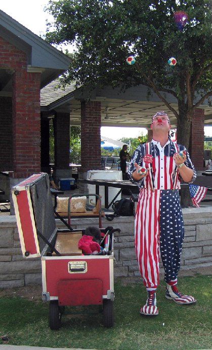 A clown in a red white and blue outfit is juggling soap bubbles