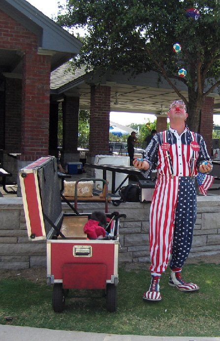 A clown in a red white and blue outfit is juggling soap bubbles