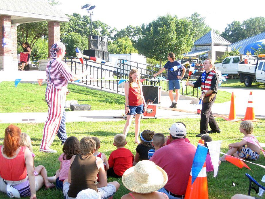 A group of people are sitting in the grass watching a clown perform