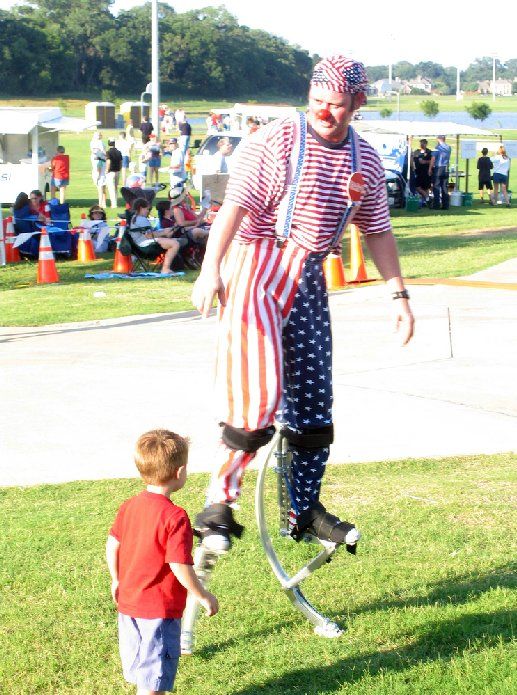 A clown on stilts is standing next to a little boy