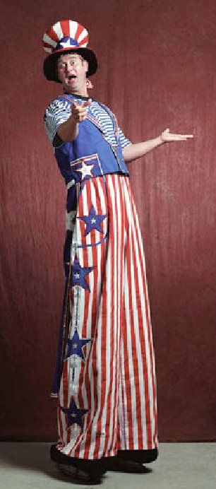 A man dressed as uncle sam is standing on stilts and pointing at the camera.