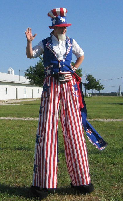 A man on stilts dressed as uncle sam is waving