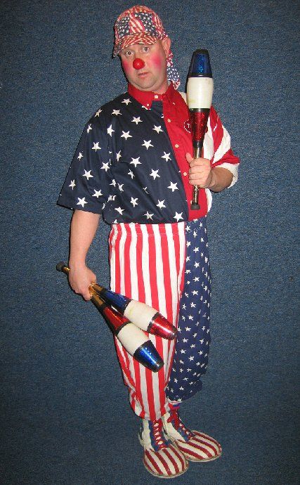 A clown in a red white and blue outfit is holding juggling pins