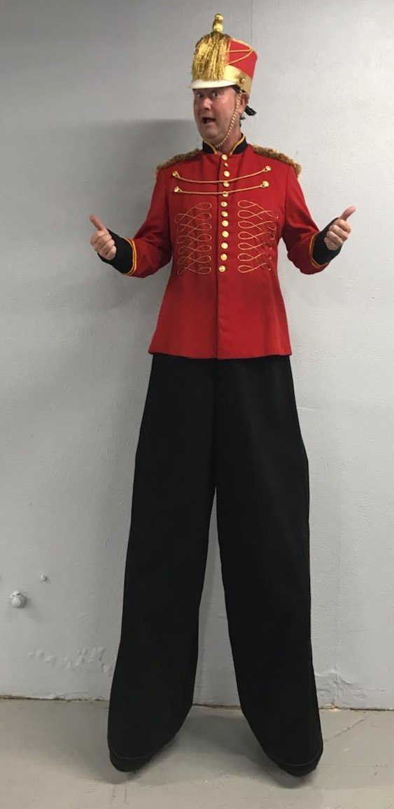 A man in a red jacket and black pants is standing on stilts.