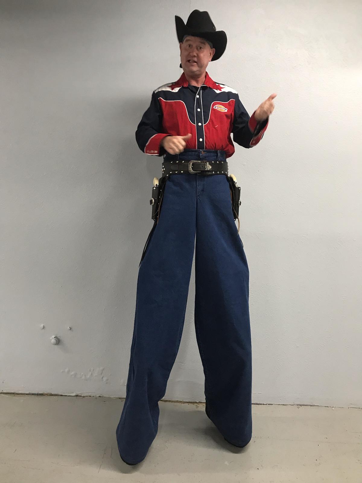 A man in a cowboy costume is standing on stilts
