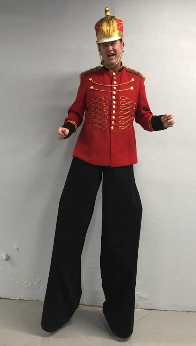 A man in a red jacket and black pants is standing on stilts.