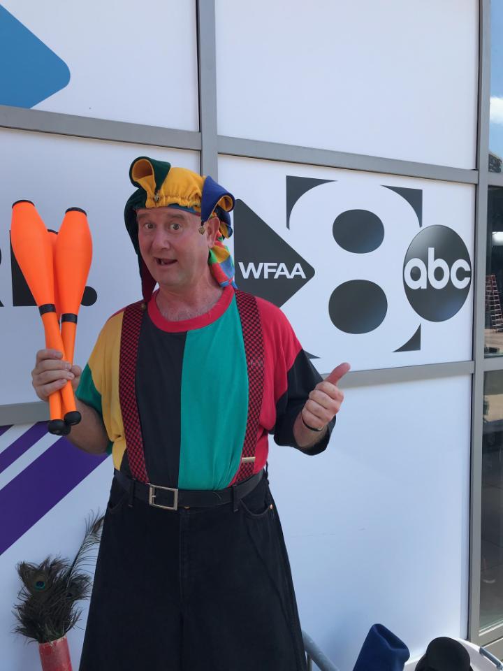 A man in a clown costume holds a pair of juggling pins in front of an abc sign