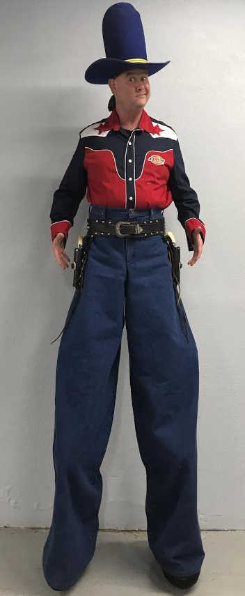 A man in a cowboy costume is standing on stilts.