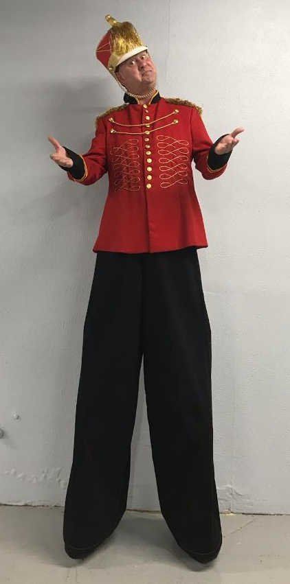 A man in a red jacket and black pants is standing on stilts.
