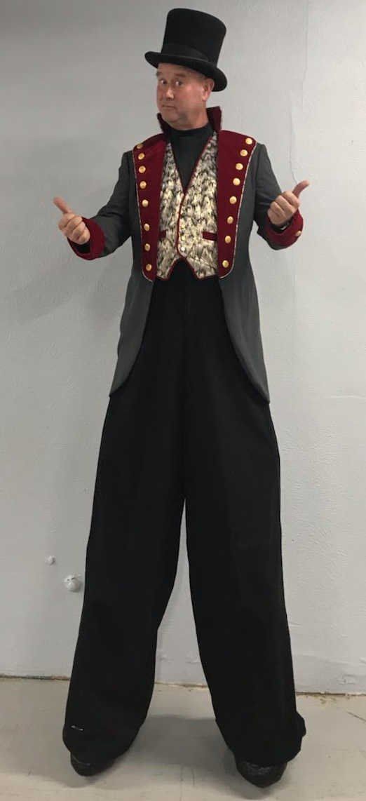 A man is standing on stilts wearing a top hat and a jacket.