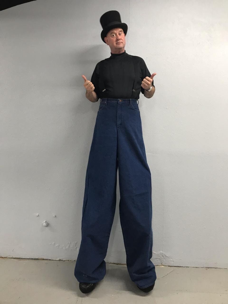 A man wearing a top hat and suspenders is standing on stilts.
