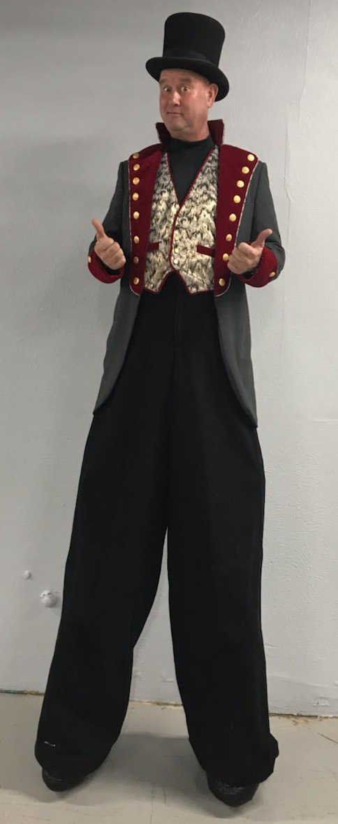 A man is standing on stilts wearing a top hat and a jacket.